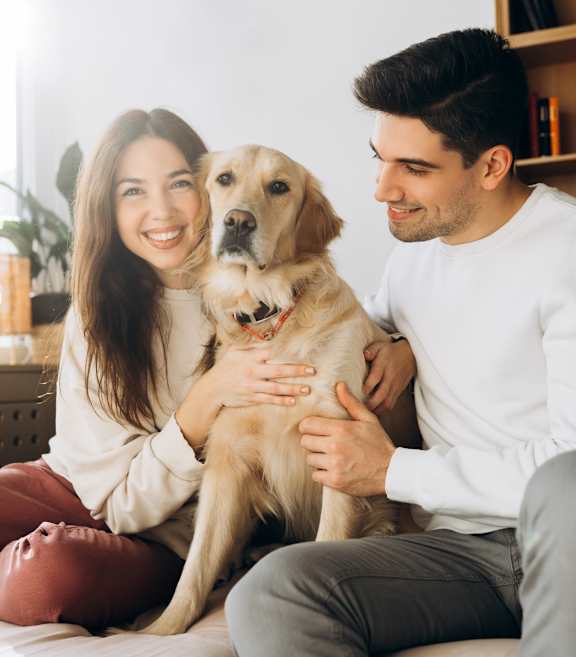 A man and woman sitting on a couch with a dog between them.