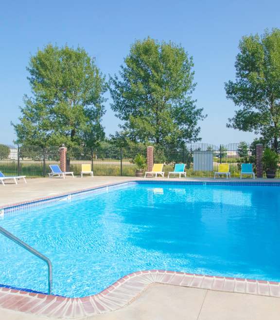 A large blue swimming pool surrounded by trees and lounge chairs.