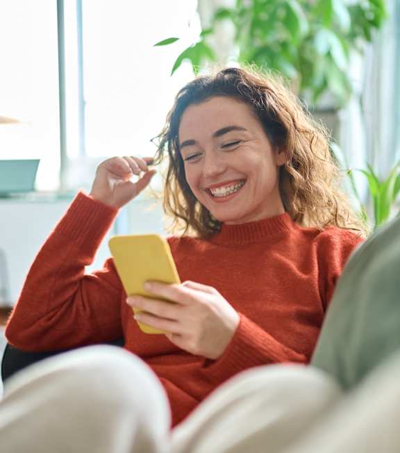 Woman Smiling while Laying on Couch and Looking at Phone