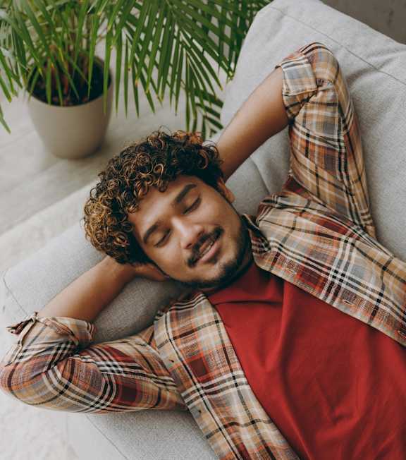 Man Wearing Plaid Shirt Laying on Couch Smiling
