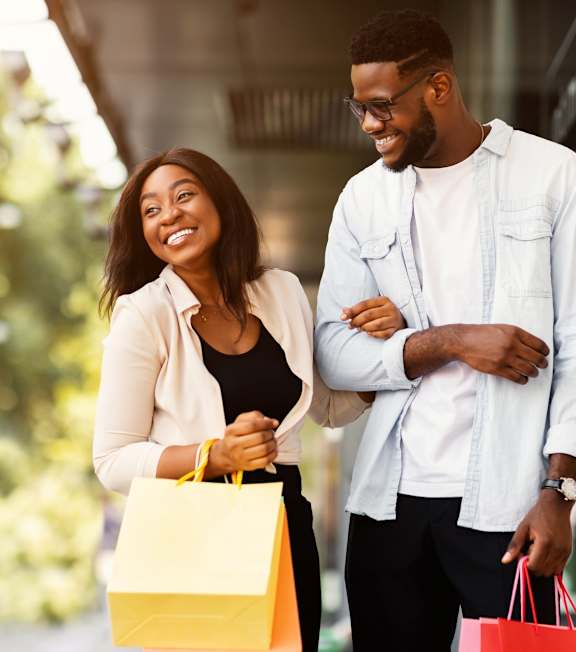 A man and woman are standing outside a store holding shopping bags.