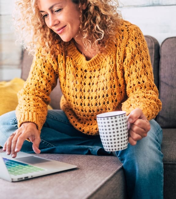 Woman Sitting on Couch while Holding Coffee Cup and Working on Laptop