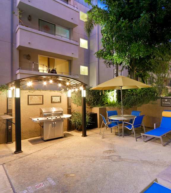 A patio with chairs and a table is surrounded by buildings at Palm Royale Apartments, Los Angeles
