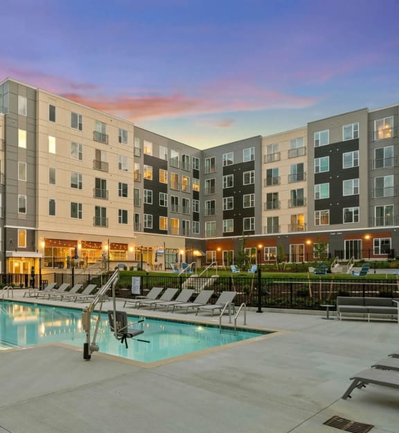 an apartment building with a swimming pool at dusk at Metropolis Apartments in Glen Allen, VA