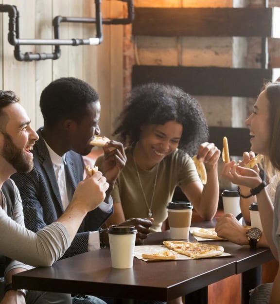 Friends Sitting Around Table Eating Pizza and Laughing