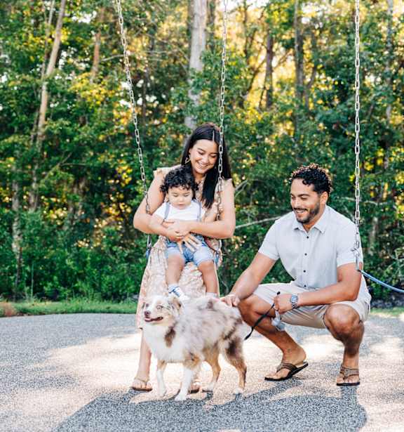 A family of three with a dog sitting on a swing in a forest.