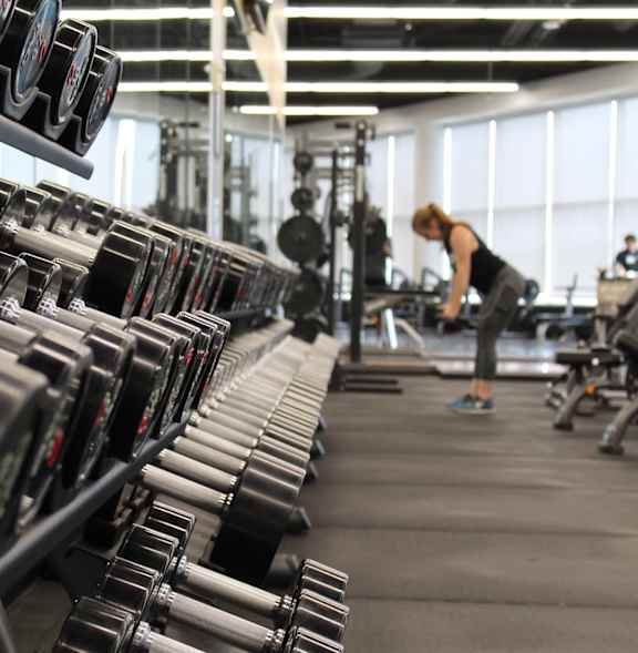 A woman is working out in a gym with a rack of dumbbells.