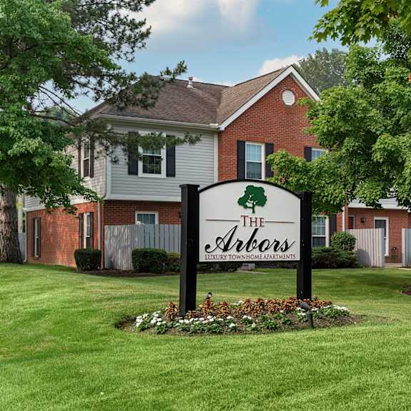 A sign for The Arbors is in the foreground of a grassy area.