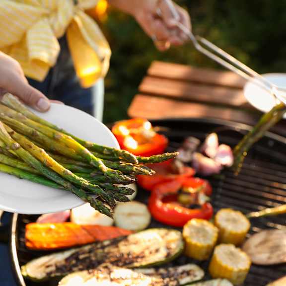A person is grilling vegetables on a barbecue.