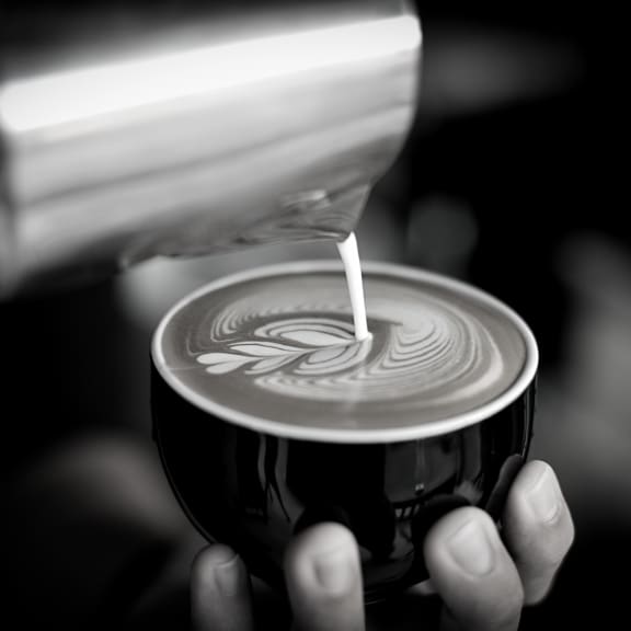 a person pouring milk into a cup of coffee at King West One, Montana