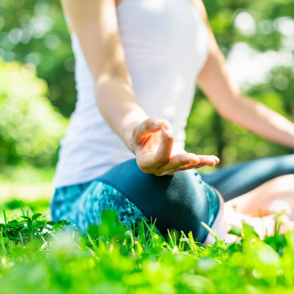 A person is sitting cross-legged on the grass in a meditative pose.
