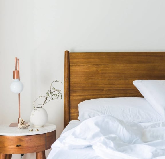 Model Bedroom with Wood Bed Frame and White Bedding Next to Wood Nightstand