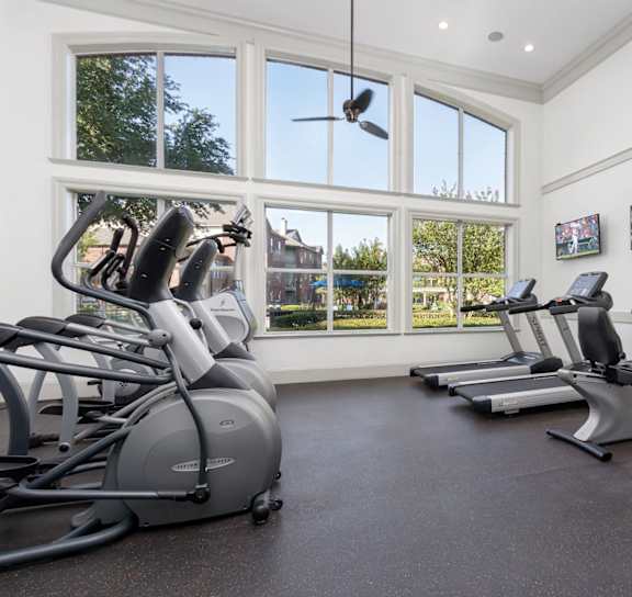 A gym with a row of stationary bikes and a fan.