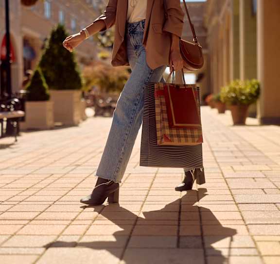 A woman is walking down a sidewalk carrying a striped bag.