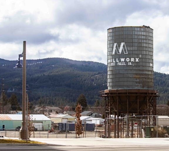 A large metal tank with the letters "M" and "Allwork" on it is situated in a parking lot.
