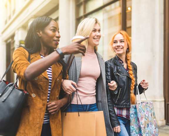 Three women are standing on a street, one of them is holding a cup.