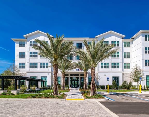 A large white building with a glass entrance and two palm trees in front. at Altis Twin Lakes Apartments, Kissimmee, FL 34744