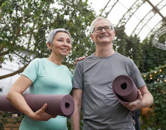 a man and a woman holding yoga mats in a greenhouse