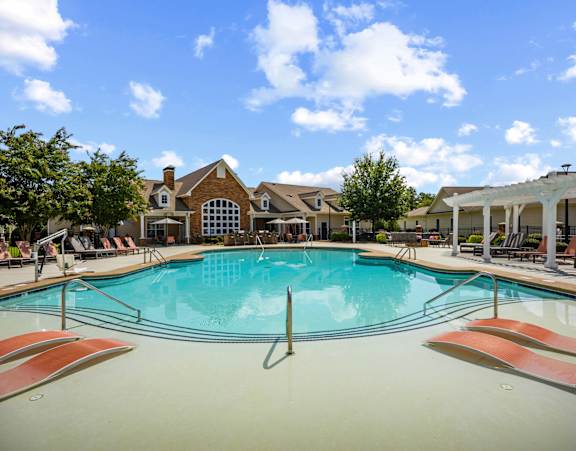 A large swimming pool with lounge chairs and a house in the background.