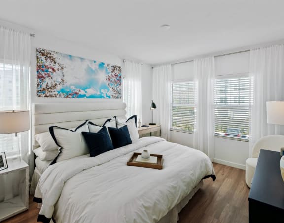 A bedroom with a large bed, a painting on the wall, and a nightstand with a lamp. at Altis Twin Lakes Apartments, Kissimmee, FL 34744