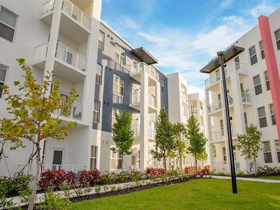 A row of modern apartment buildings with balconies and trees in front.