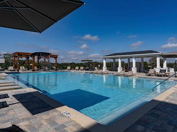 A large outdoor swimming pool with a tiled edge and a shaded area with lounge chairs at The Waverly at Winter Haven Apartments, Winter Haven, 33884