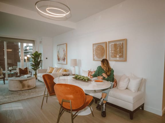a woman sits at a dining table in a living room with a white couch