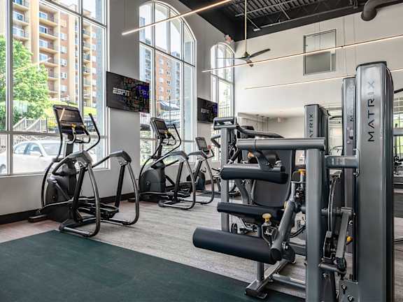 a gym with weights and cardio equipment in a building with large windows