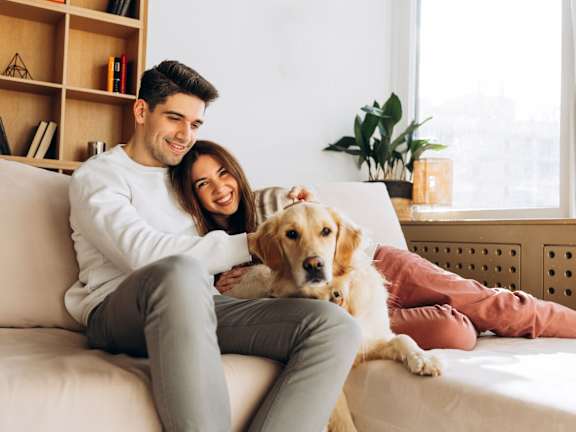 A man and woman are sitting on a couch with a dog between them.