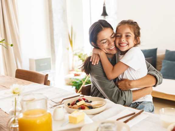 A woman and a child are hugging at a breakfast table.