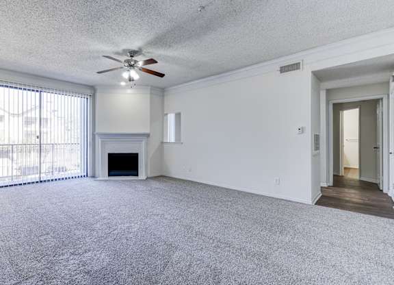 A large living room at Saxony at Chase Oaks Apartments in Dallas, TX, featuring built-in shelving above the fireplace, a ceiling fan and carpeted floors.