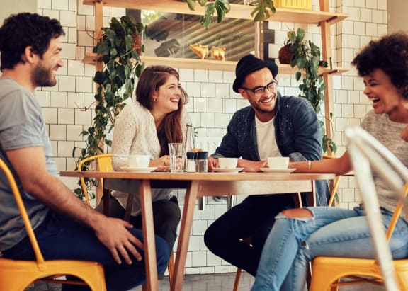 Friends Sitting Around Table in Restaurant Together Smiling
