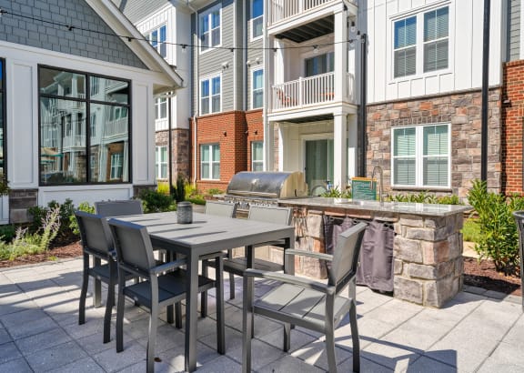 a patio with a table and chairs and a grill in front of a building at Artistry at Winterfield Apartments, Virginia