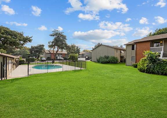 A grassy backyard with a pool and houses in the background.