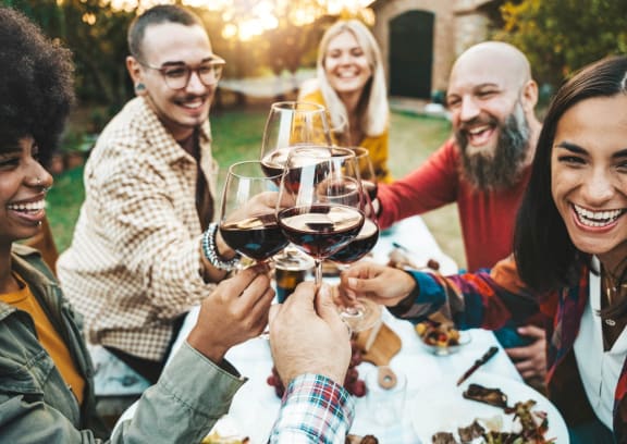 Friends Sitting Around Table Smiling while Holding Glasses of Wine