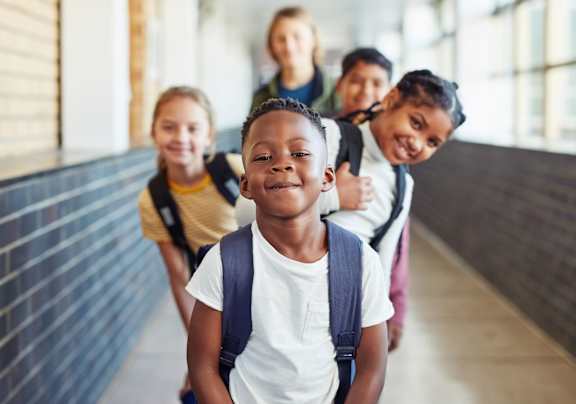 a group of young boys and girls standing in a hallway with their backpacks on