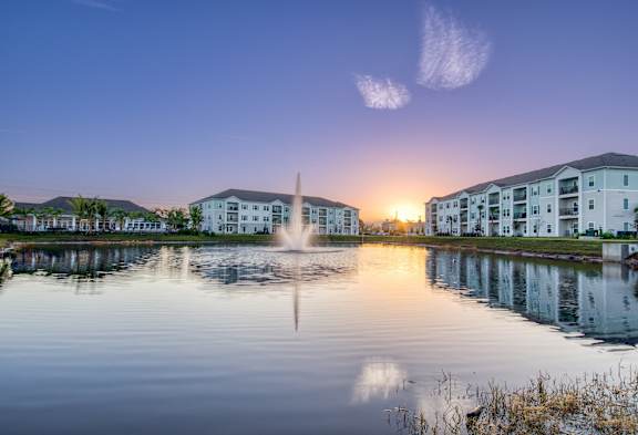A serene lake with a fountain in the middle surrounded by buildings.