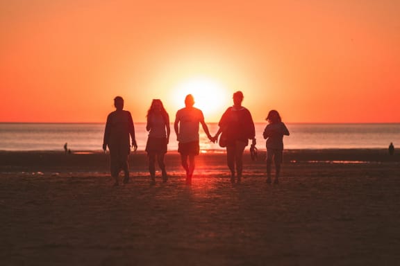 a group of people walking on the beach at sunset
