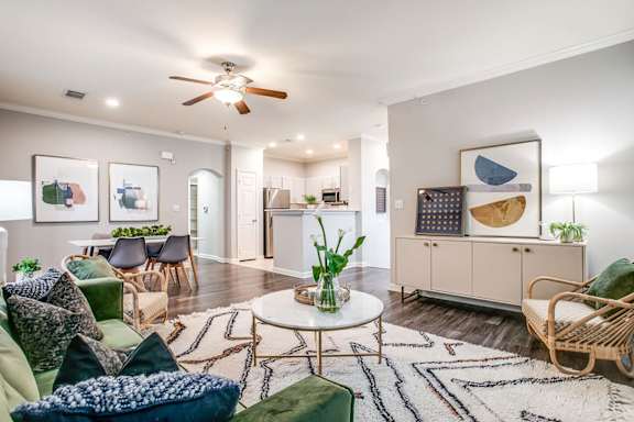 a living room with a ceiling fan and a kitchen in the background