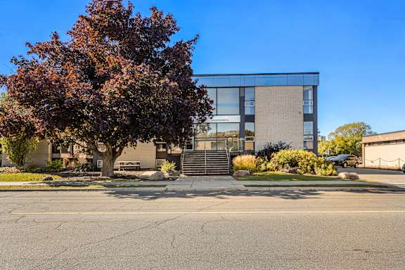 A tree with red leaves is in front of a building with a glass facade.