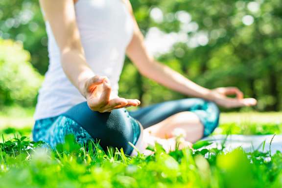 A person is sitting cross-legged on the grass in a meditative pose.