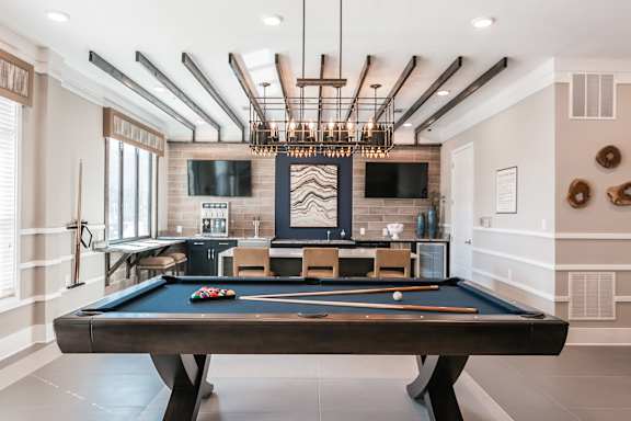 A pool table is in the middle of a room with a TV and a bar.