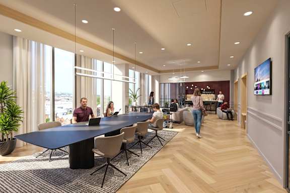 A modern office space with people working at tables and a woman walking by.