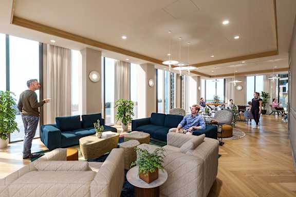 A group of people are sitting and standing in a modern, well-lit room with blue couches and plants.
