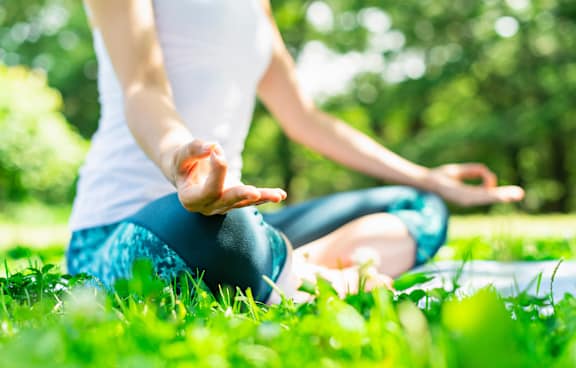 A person is sitting cross-legged on the grass in a meditative pose.