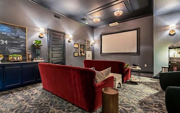A living room with a red couch and a grey car poster on the wall.
