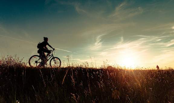 A person riding a bike on a grassy hill during sunset.