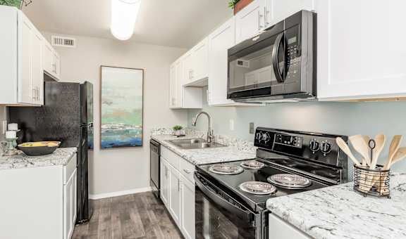 A kitchen with a black fridge, black microwave, and black stove.