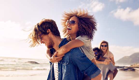 A man is carrying a woman on his back on a beach.