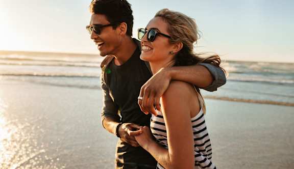 A man and a woman are standing on a beach, with the man holding the woman's hand.